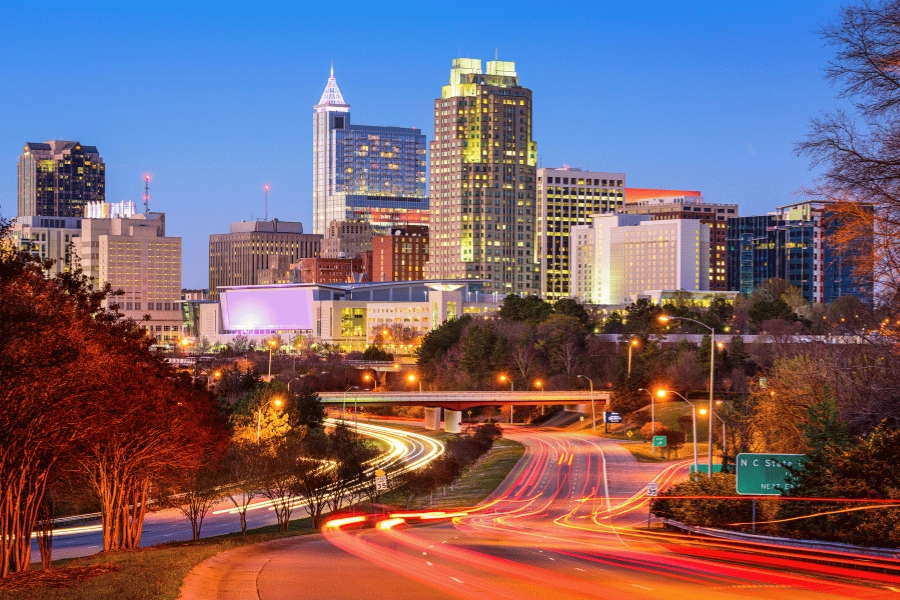 view of downtown raleigh lit up at night with road signs and car break lights
